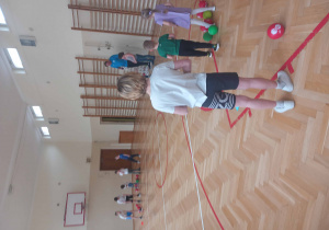 Uczniowie i przedszkolaki w sali gimnastycznej wykonują proste ćwiczenia