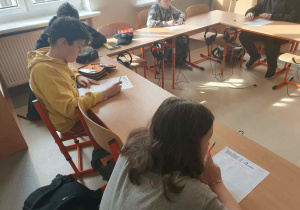 Uczniowie klas starszych pochyleni nad swoimi pracami w konkursie z języka angielskiego