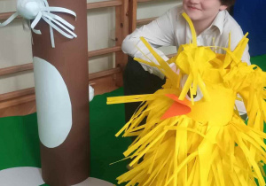 Dekoracja w postaci dużego brązowego królika i pierzastego, żółtego kurczaka z papieru a pomiędzy nimi uśmiechnięty uczeń