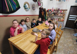 w izbie- dzieci siedzą przy drewnianym stole, na ścianach kolorowe elementy stroju ludowego, rękodzieło, a pod sufitem tradycyjne, kolorowe pająki