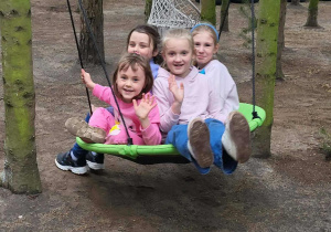 Cztery dziewczynki huśtają się na huśtawce między drzewami na placu zabaw