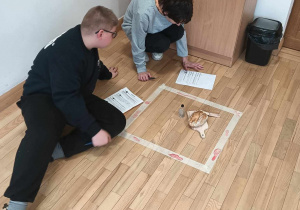 Chłopcy pracują z tekstem, przed mini dowód zbrodni w postaci deski do krojenie i pieczywa na niej