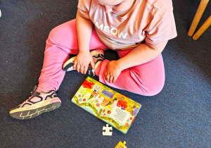 Dziewczynka ogląda książeczkę, której ilustracje składa się z puzzli