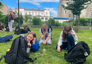 Na trawie uczniowie leżą lub siedzą za swoimi plecakami