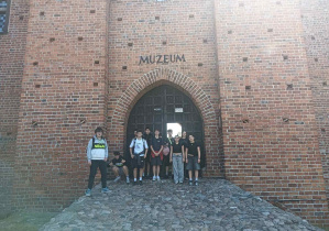 Uczniowie na tle bramy wejściowej do zamku, na ceglnej ścianie napis "Muzeum"