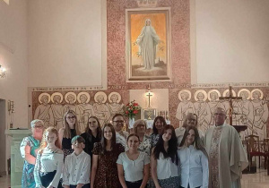 Wspólne zdjęcie na tle witraża i obrazu Matki Bożej Królowej Pokoju