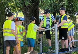 W kamizelkach odblaskowych dzieci bawią się na placu zabaw