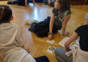 Warsztaty - dzieci siedzą na parkiecie i słuchają prowadzącego