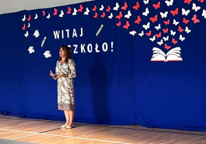 Pani dyrektor przemawia w tle dekoracja - otwarta książka z której wyfruwają białe i czerwone motyle