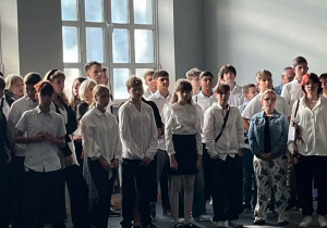 Młodzież uczestnicząca w uroczystości za nimi wysokie zwieńczone łukiem okno