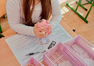 Uczennica nad pracą obok różowe koszyczki z pomocami do zajęć
