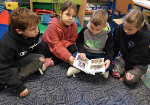 Uczniowie na dywanie starają się czytać książkę palcami