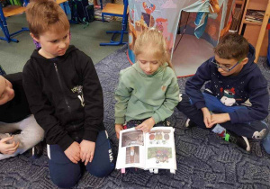 Uczniowie na dywanie starają się czytać książkę palcami